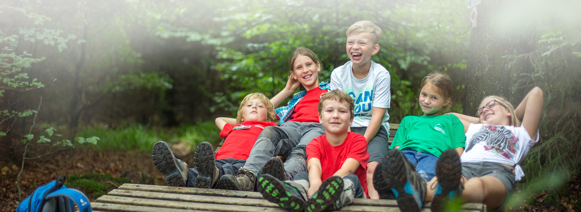 Eine Kindergruppe sitzt auf einer Holzliege und lacht in die Kamera.