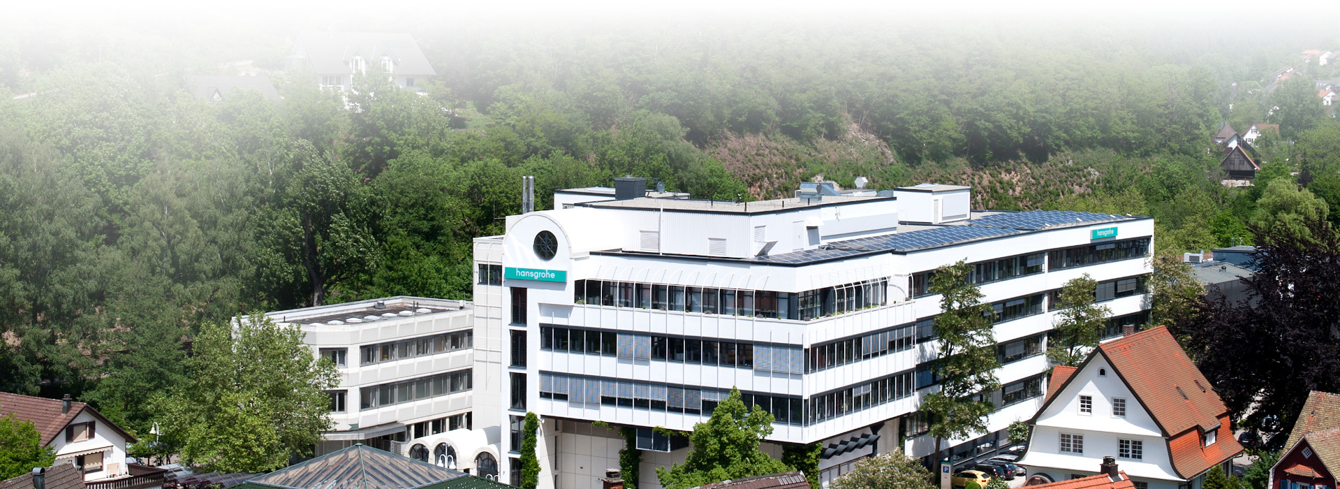 Hauptgebäude des Firmensitzes der Hansgrohe SE in Schiltach. Das Firmenlogo ist außen am Gebäude zu erkennen. Wald im Hintergrund. 