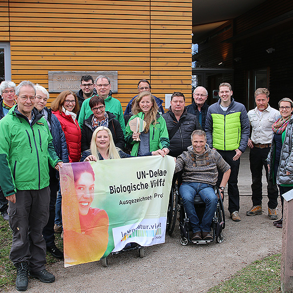 Eine Gruppe Menschen stehen für ein Gruppenbild zusammen. Einige halten ein Plakat mit dem Aufdruck "UN-Dekade Biologische Vielfalt. Ausgezeichnetes Projekt". Einer der Männer sitzt im Rollstuhl.