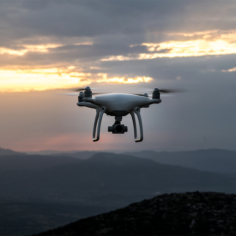 Eine Drohne schwebt vor einem abendlichen Wolkenhimmel über Berggipfeln.