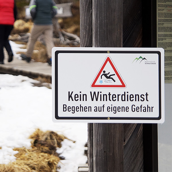 Schild mit Aufschrift "Kein Winterdienst Begehen auf eigene Gefahr" und einem Piktogramm eines ausrutscheneden Männchens.