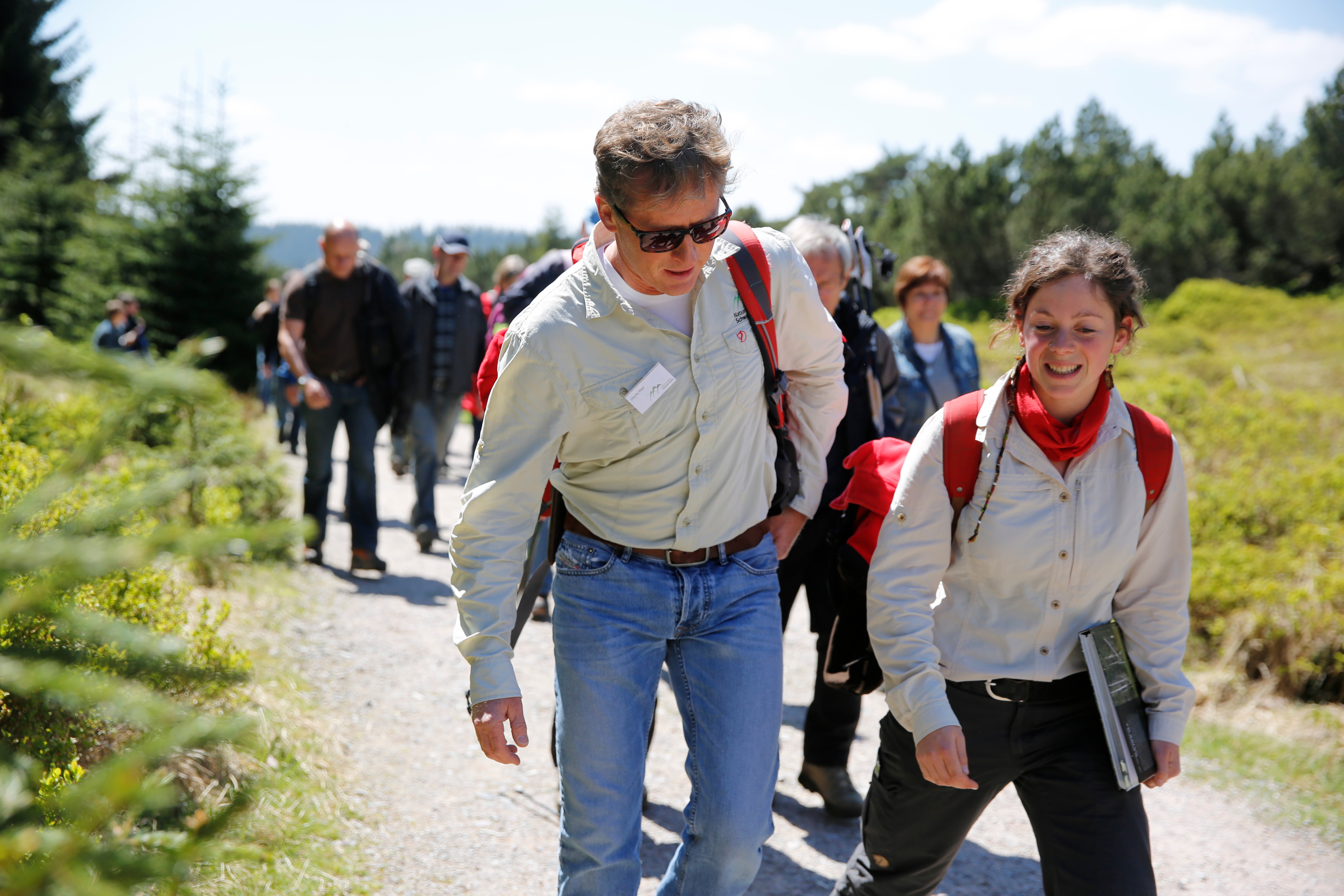 Zwei Ranger, ein Mann und eine Frau, laufen vor einer Gruppe Besucher her. 