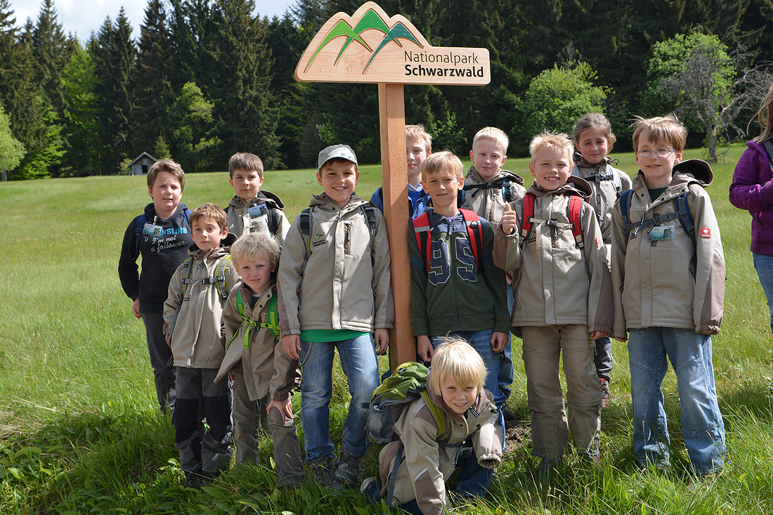 Eine Gruppe Kinder steht um ein Nationalparkschild an einem Pfosten.