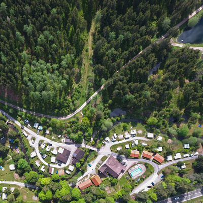 Blick aus der Luft auf den Naturcampingplatz Langenwald. Auf der Fläche des Campingplatzes stehen verschiedene Zelte, die Stellplätze sind durch eine Straße verbunden.