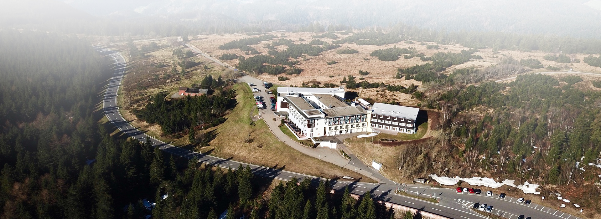Drohnenbild des Nationalpark-Hotels Schliffkopf. Das große Hotel steht am Rand der Grinde, einer halboffenen Weidenlandschaft. Links des Hotels ist noch Wald. Direkt unterhalb des  Hotels verläuft eine große Straße, die B500.