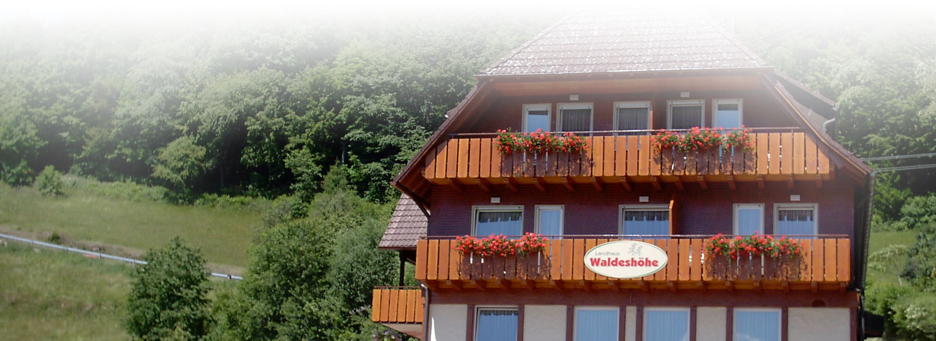 Ein Haus im Schwarzwaldstil, an den Balkonen hängen Blumenkästen. An einem Balkon hängt ein Schild mit der Aufschrift Waldeshöhe