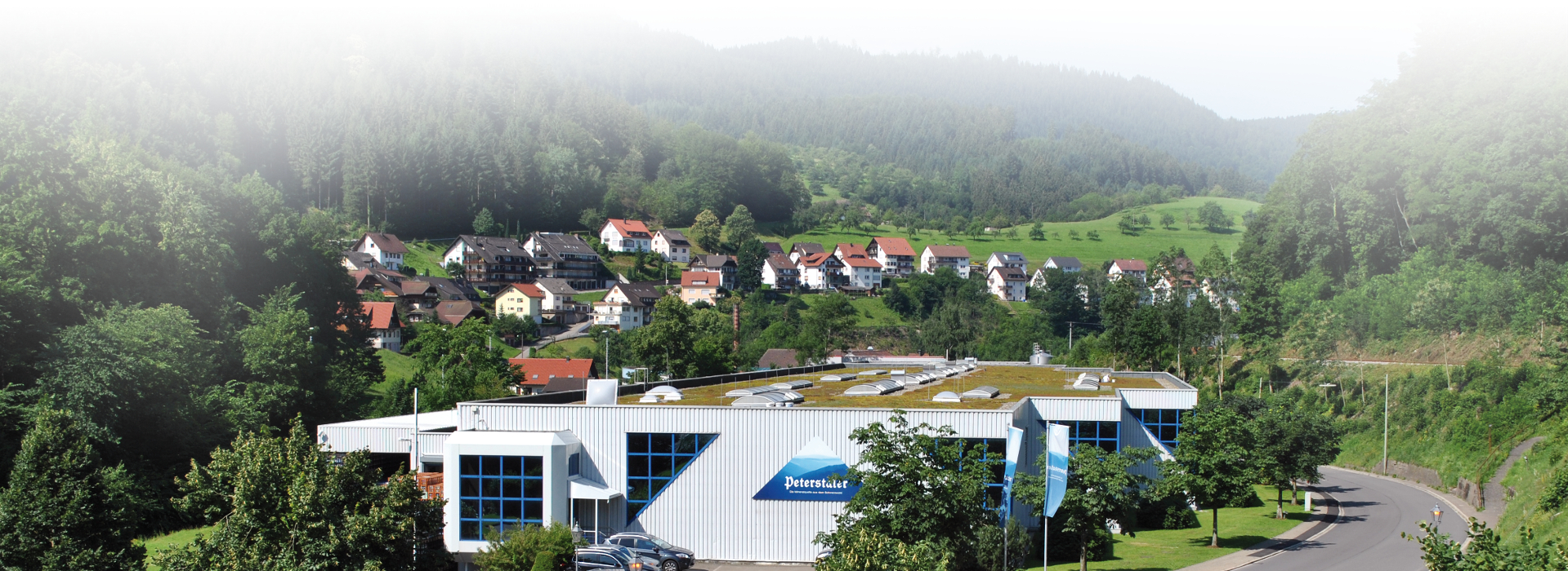 Hauptgebäude des Firmensitzes der Peterstaler Mineralquellen GmbH in Bad Peterstal. Das Firmenlogo ist außen am Gebäude zu erkennen. Wald im Hintergrund. 