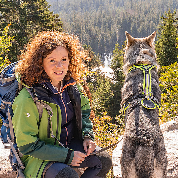 Rangerin sitzt lächelnd am Wilden See Blick mit ihrem Hund