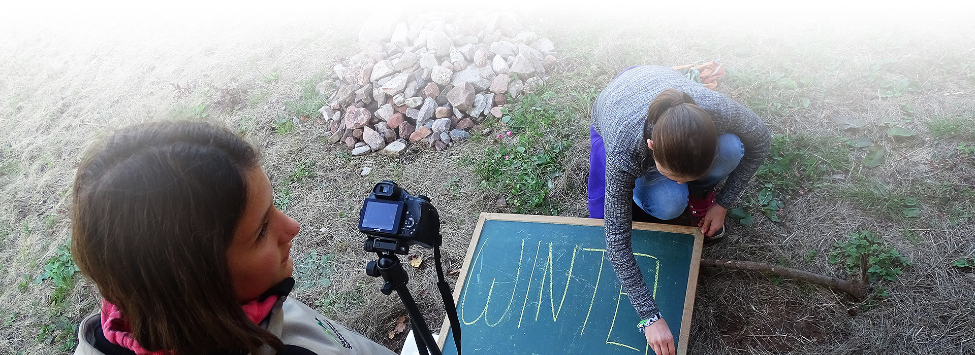 Juniorranger am Filmset. Ein Mädchen schreibt mit Kreide auf eine Tafel. Links im Bild steht ein weiteres Mädchen mit Kamera.