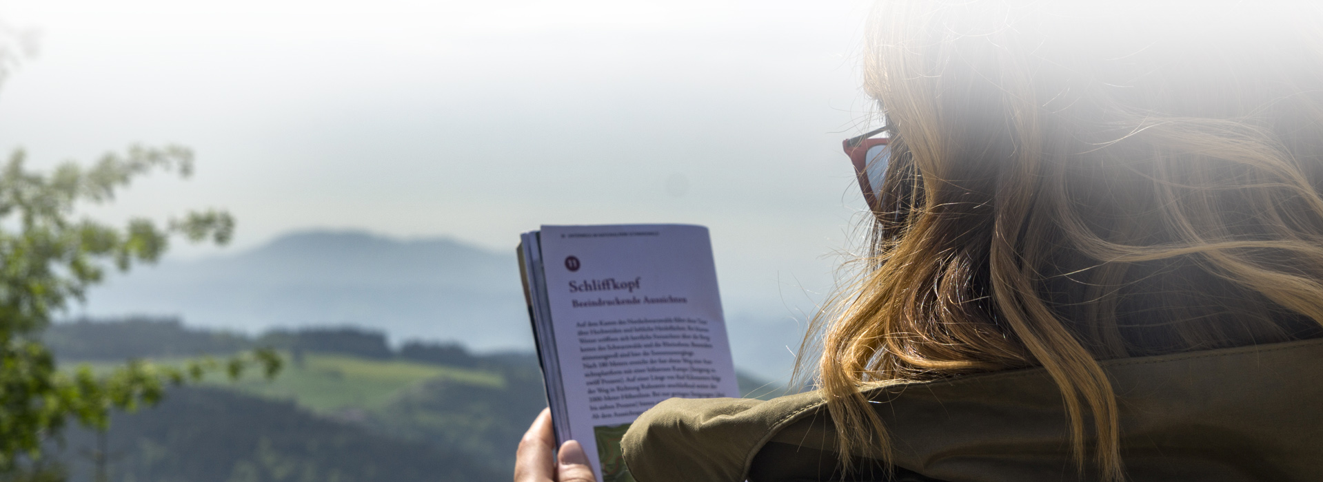 Eine Wandererin hält einen Nationalparkflyer in der Hand und liest ihn. 