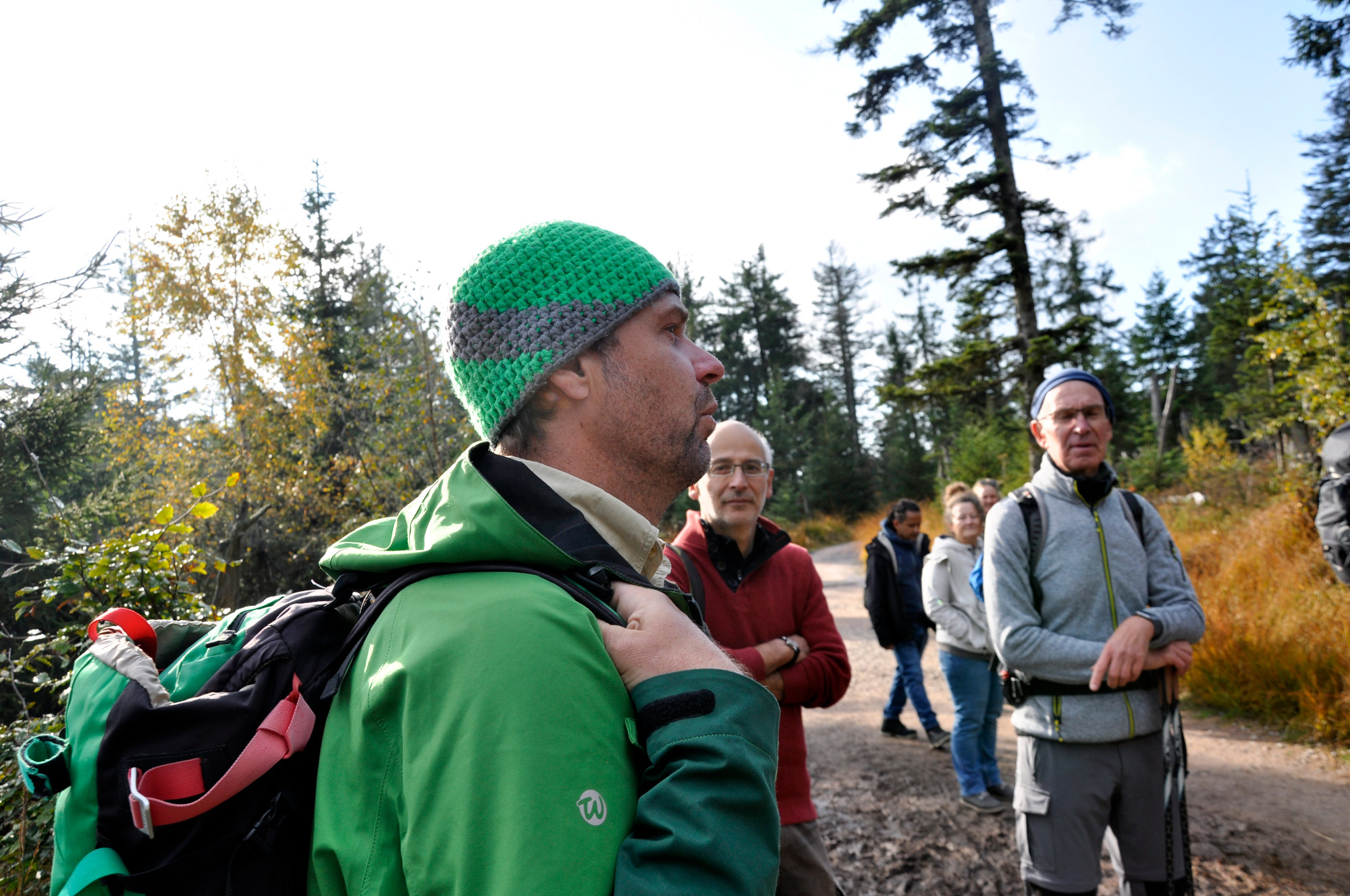 Ein Ranger mit bunter gehäkelter Mütze und herbstlich warmer, grüner Outdoorkleidung steht in einer Gruppe MEnschen und erklärt etwas.