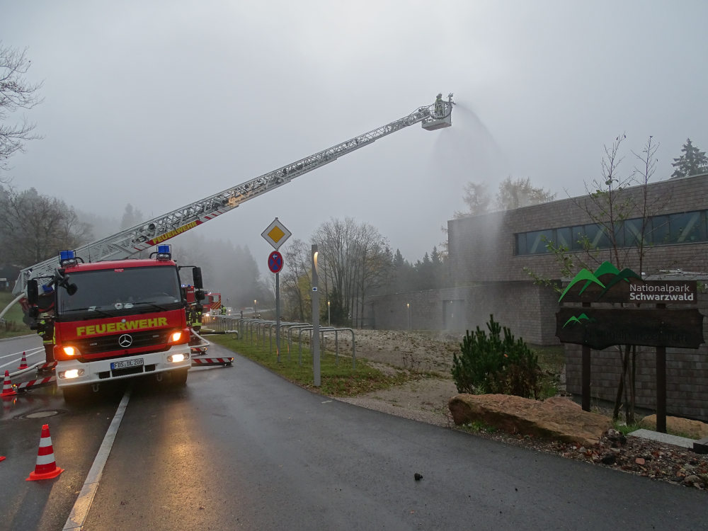 Ein Feuerwehrfahrzeug mit ausgefahrener Leiter steht vor einem großen hölzernen Gebäude.