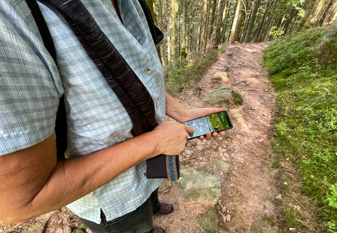 Ein Mann im karierten Hemd hält auf einem Waldweg ein Handy in der Hand. Foto: Andreas Forch