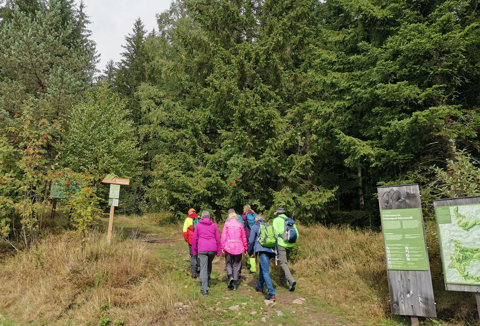 Eine Gruppe Menschen unterschiedlichen Alters und Geschlechts in Outdoorkleidung draußen im Sommer.