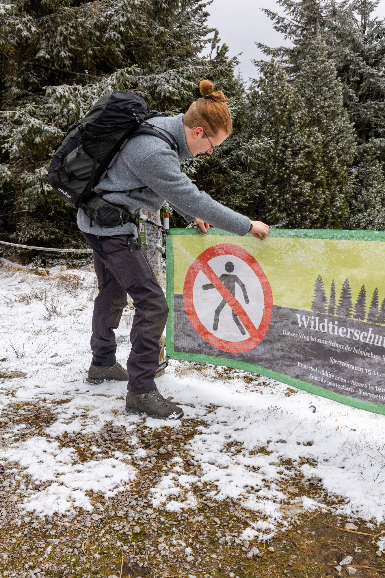 Ein junger Mann hängt in einer winterlichen Waldlandschaft ein Banner mit einem Durchgangsverbots-Symbol auf