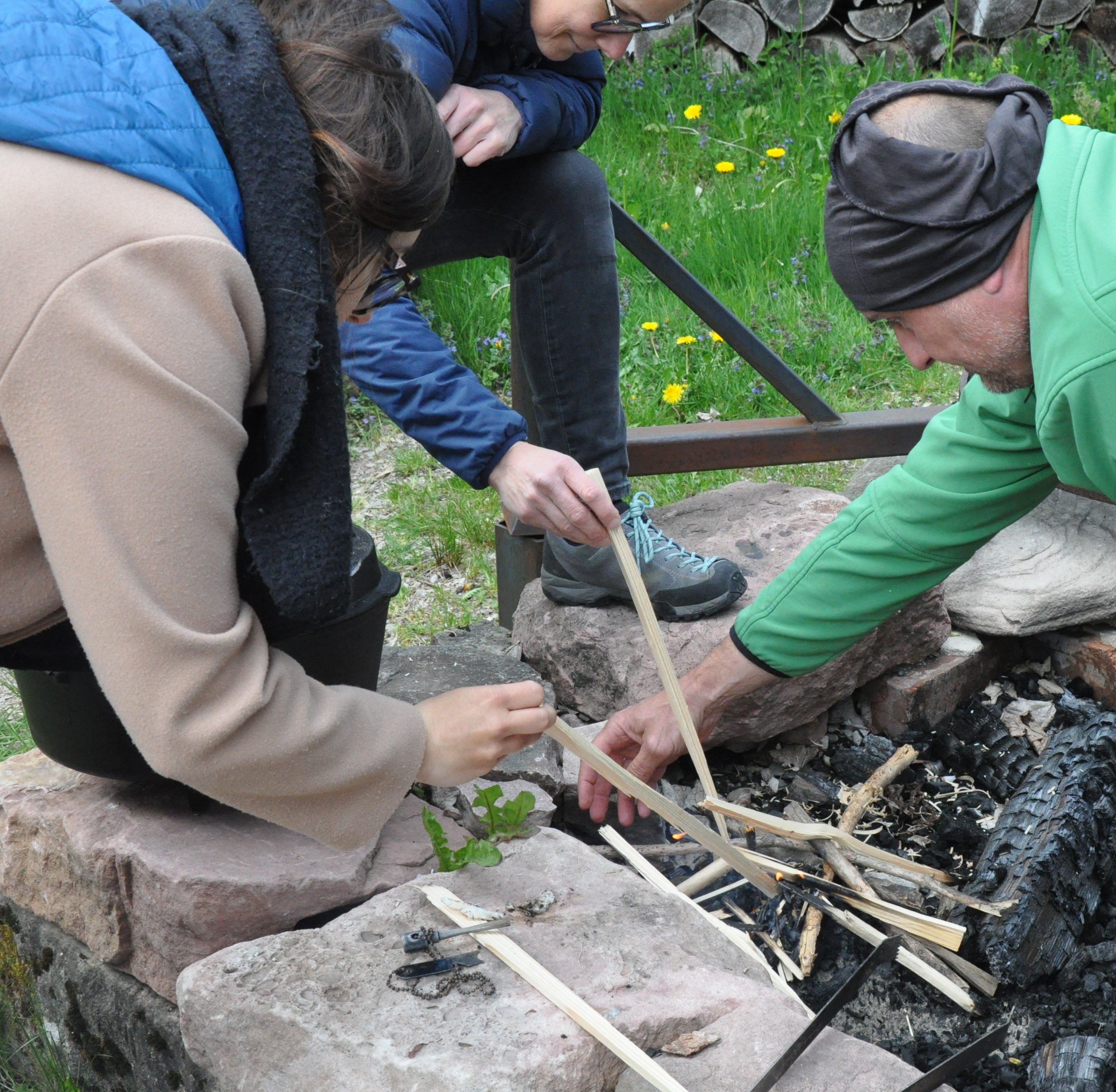 Menschen stochern mit Hölzern in einer Feuerstelle