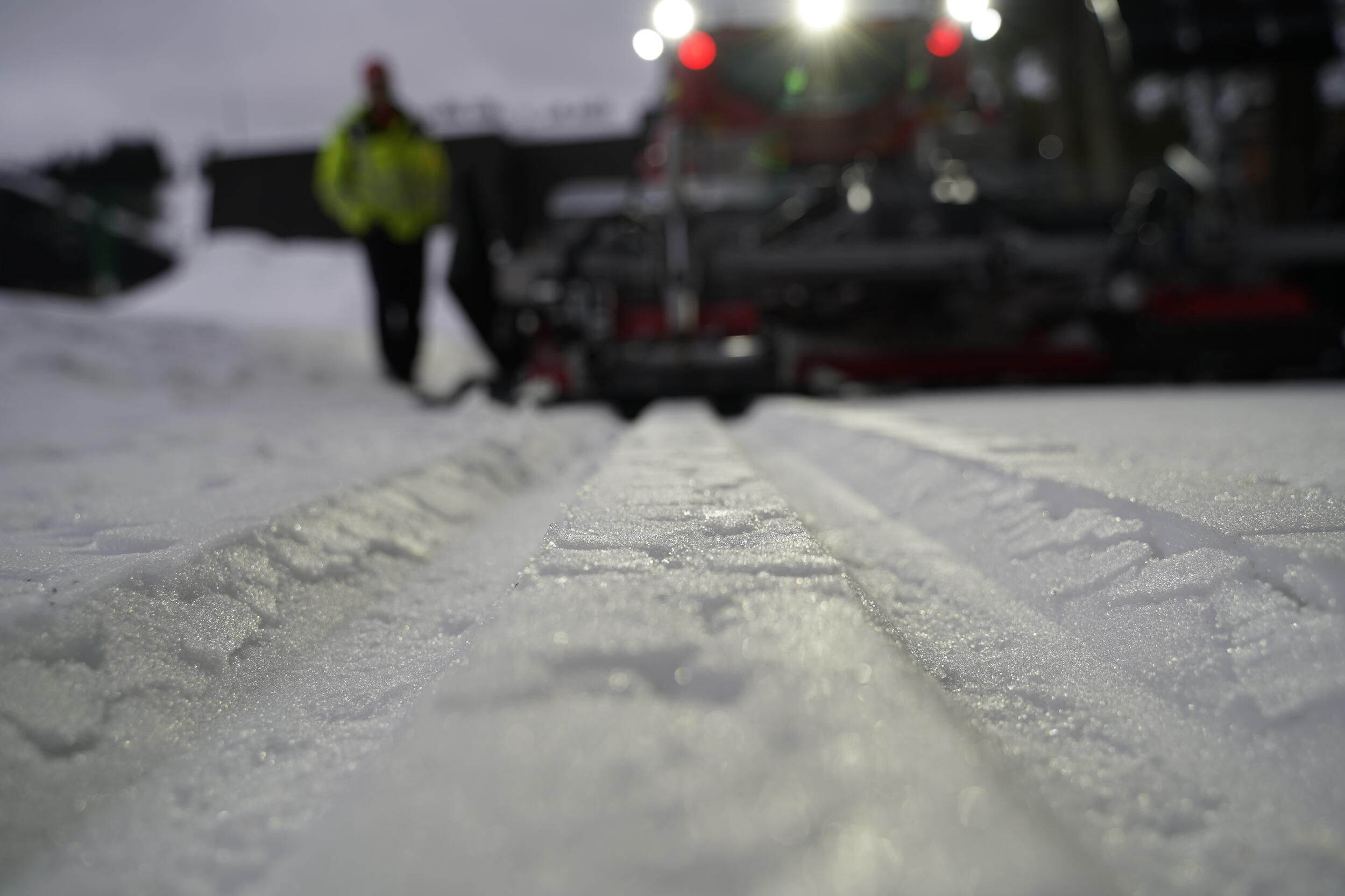 Eine Aufnahme aus der Froschperspektive: Ein dick verschneiter Weg. Der Schnee wurde ordentlich geglättet und es führen nun zwei schnurgerade Vertiefungen wie der Abdruck von Eisenbahngleisen den Weg entlang. 