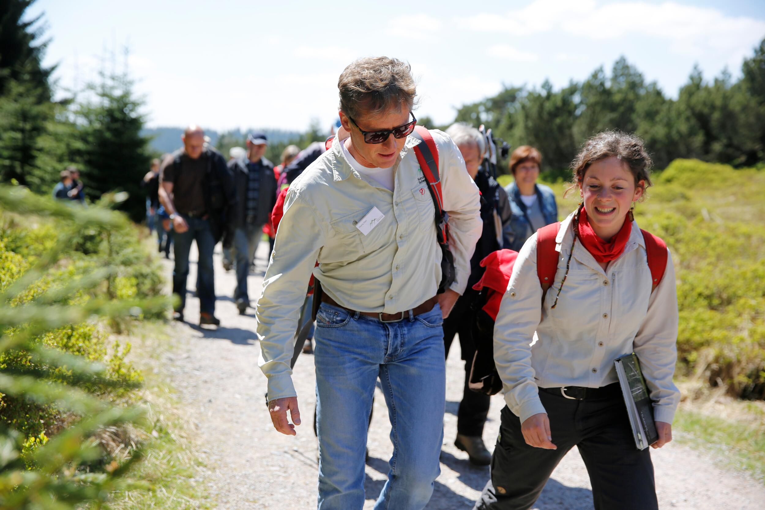 Zwei Ranger, ein Mann und eine Frau, laufen vor einer Gruppe Besucher her. 