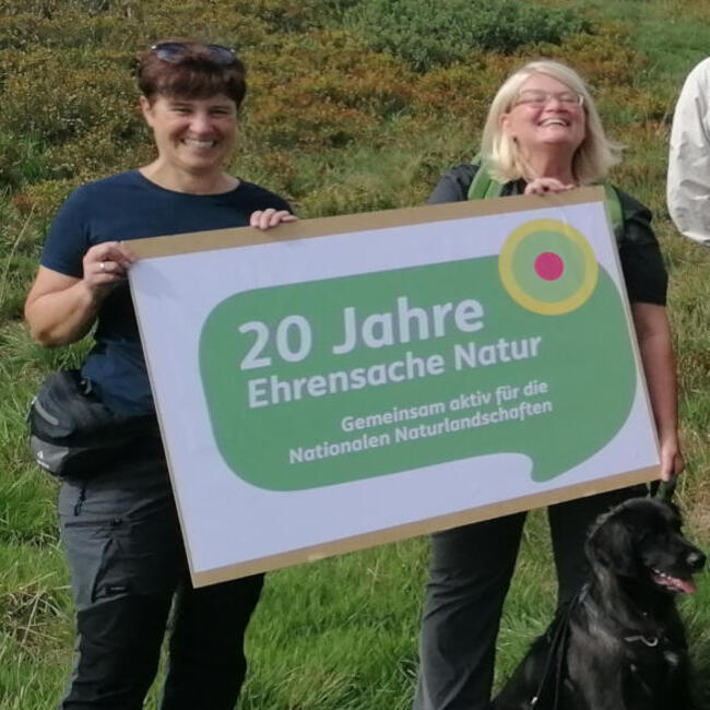 Frauen und Männer haben sich zu einem Gruppenbild in der Natur aufgestellt, zwei Frauen ganz links halten ein Schild mit dem Aufdruck: 20 Jahre Ehrensache Natur. Foto: Rolf Brökland