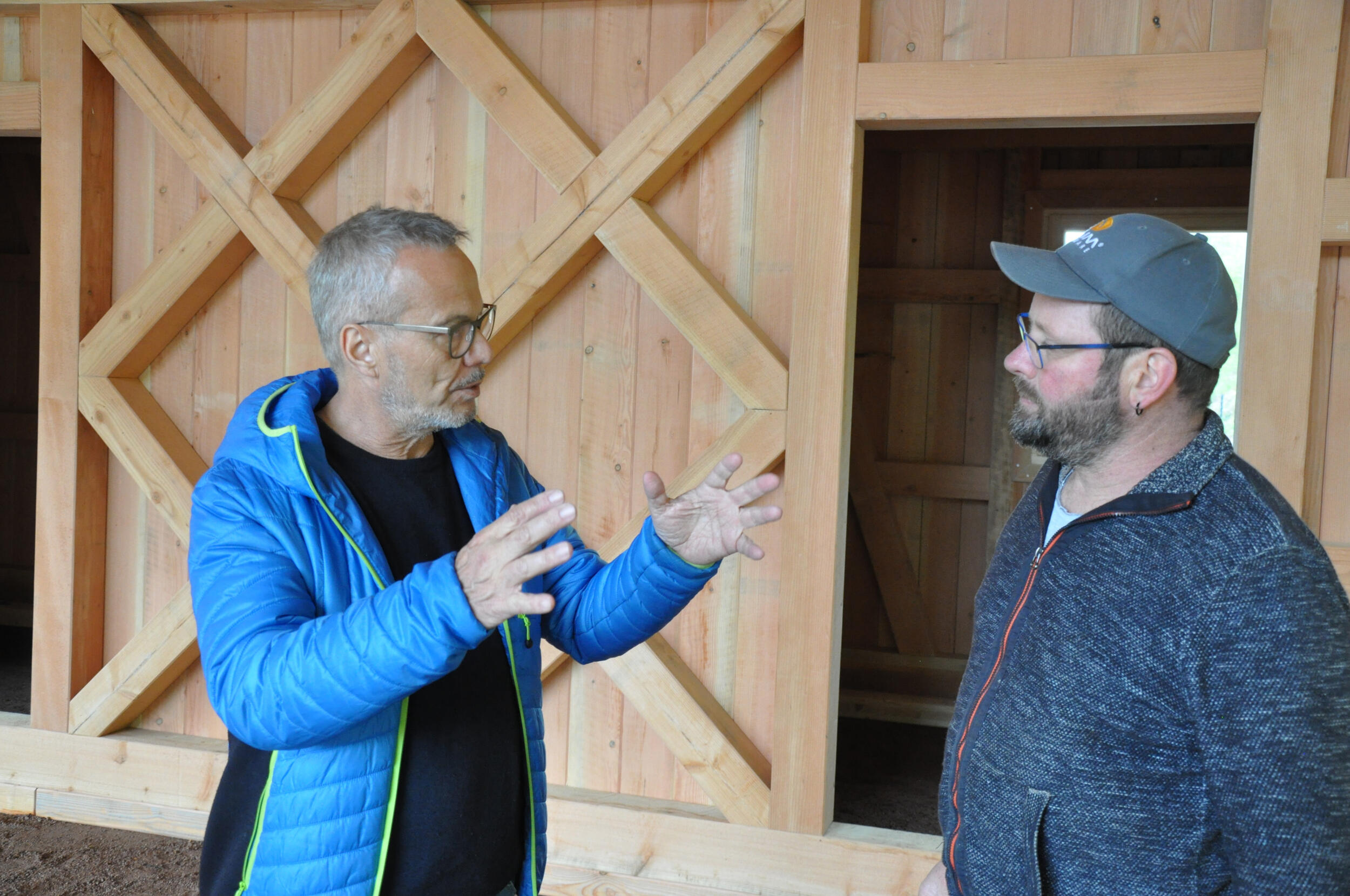 Zwei Männer stehen vor einer Hütte. Sie sprechen. Einer von ihnen gestikuliert. 