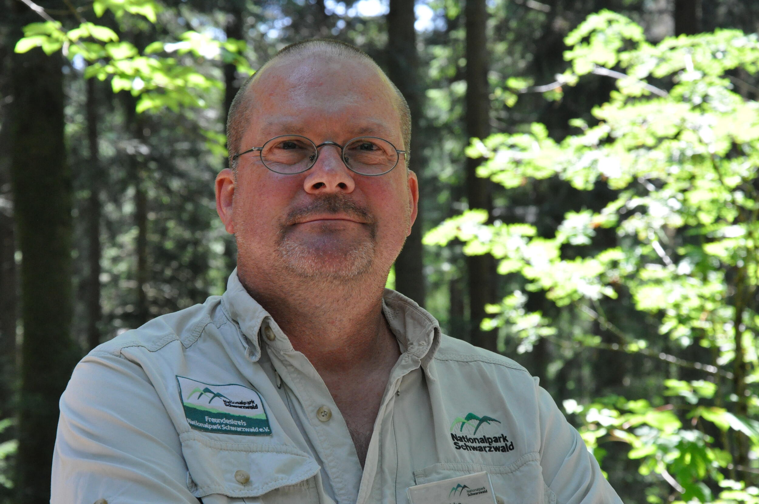 Ein Mann im beigen Hemd und einer Brille steht vor Hintergrund eines Waldes. Er sieht freundlich aus. Foto: Nina Blazon 