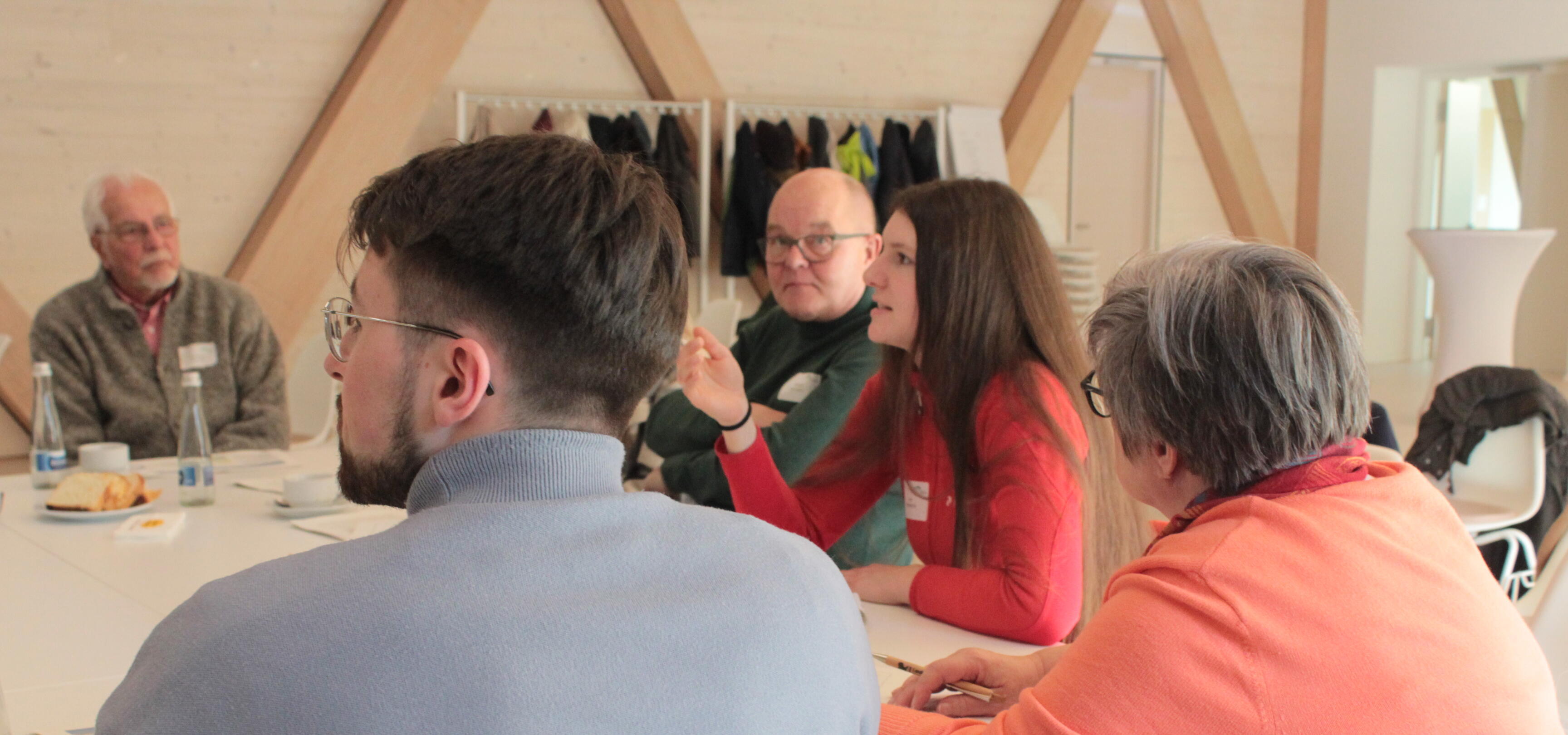 Fünf Menschen sitzen um einen Tisch und diskutieren.