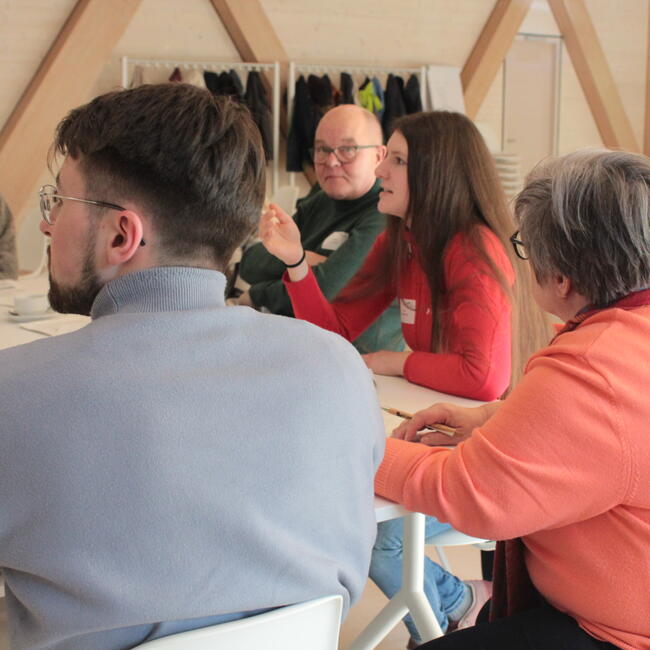 Fünf Menschen sitzen um einen Tisch und diskutieren.