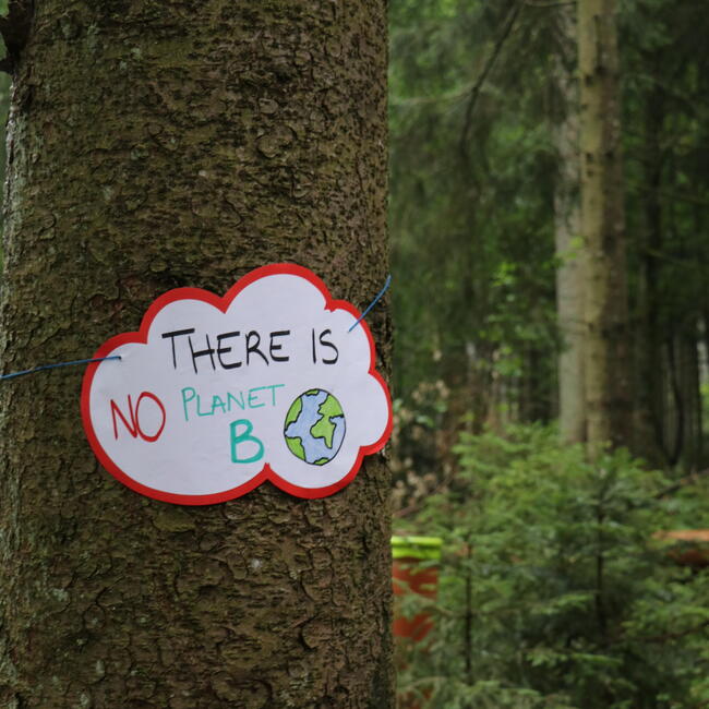 Ein Schild "There is no planet B" hängt an einem Baum im Wald