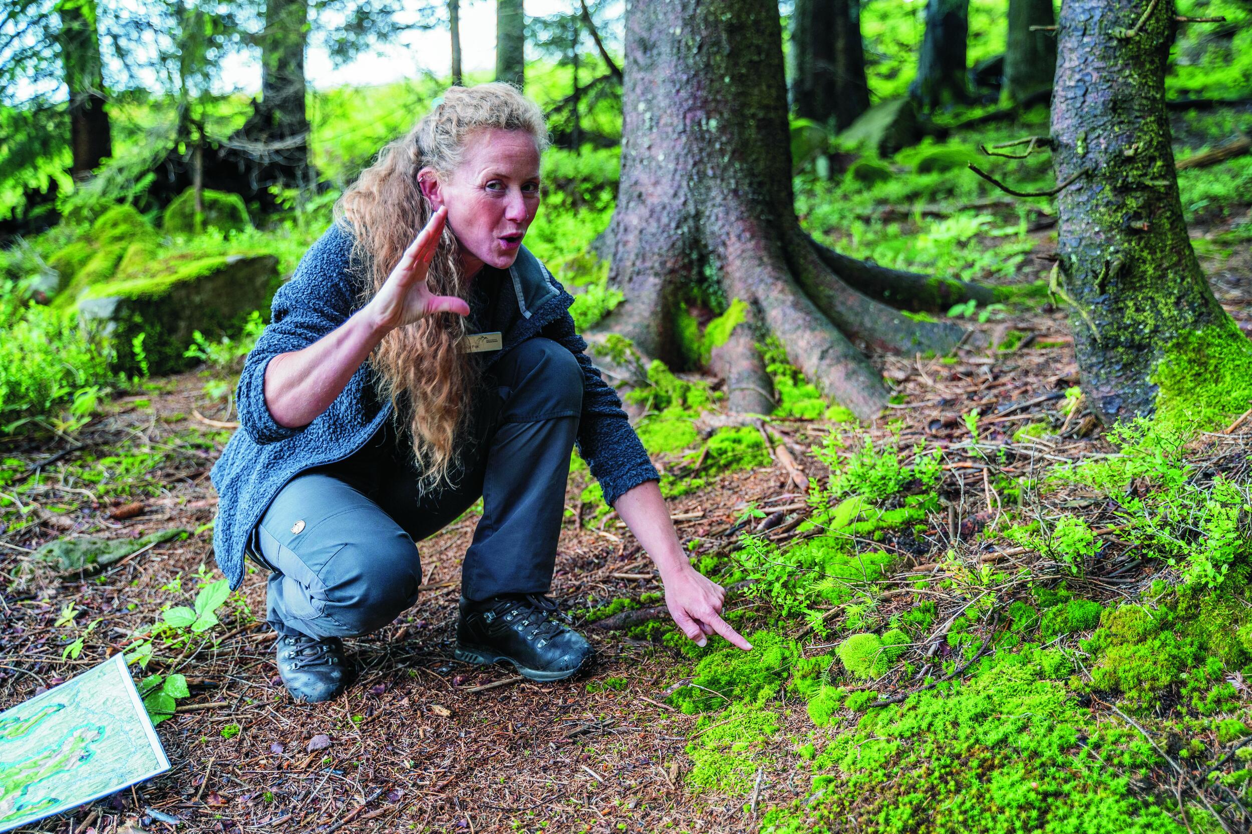 Svenja Fox zeigt etwas auf dem Waldboden und mit einer Gebärde.