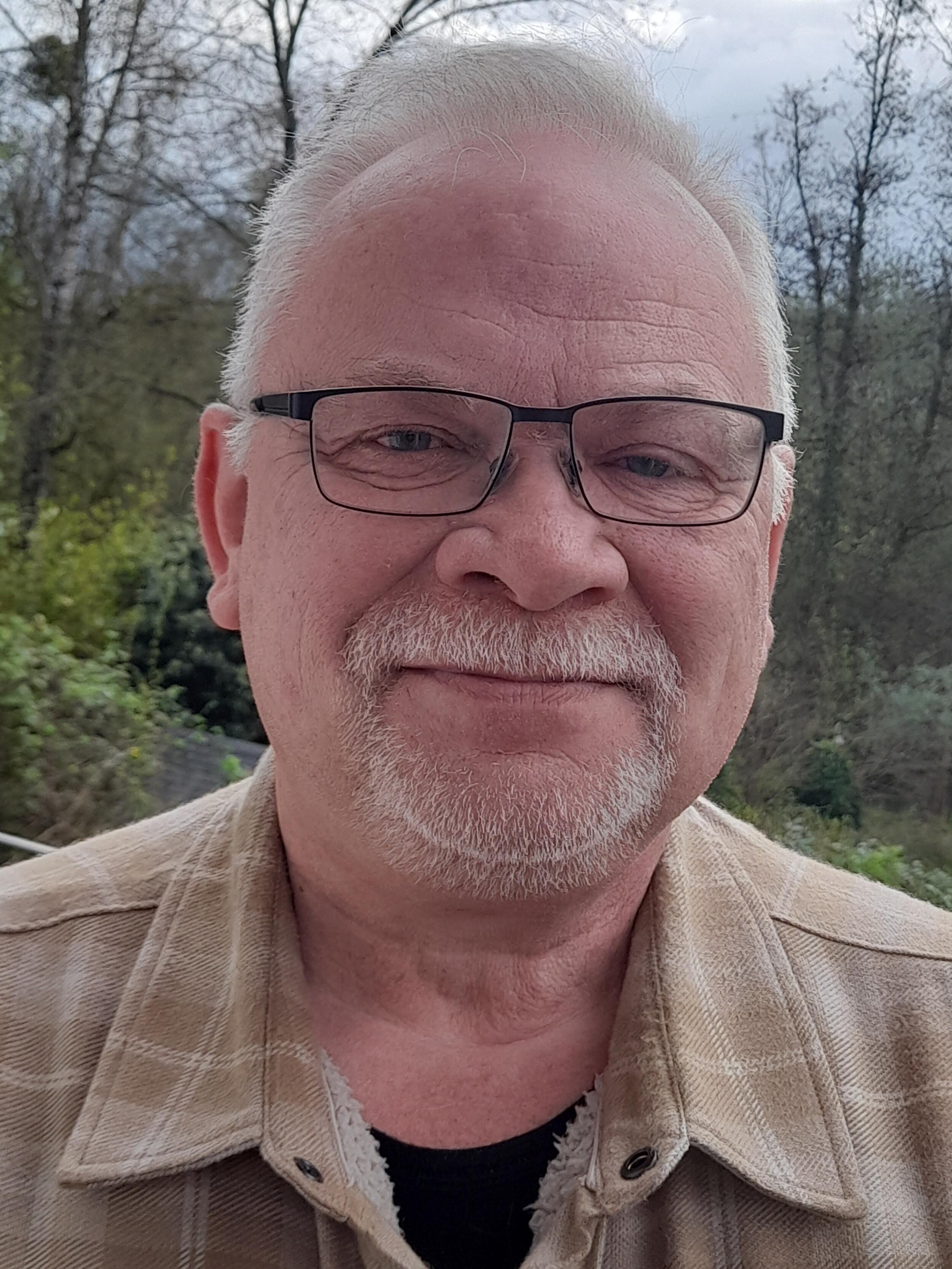 Ein Mann mit einer schwarzen Brille lächelt in die Kamera. 