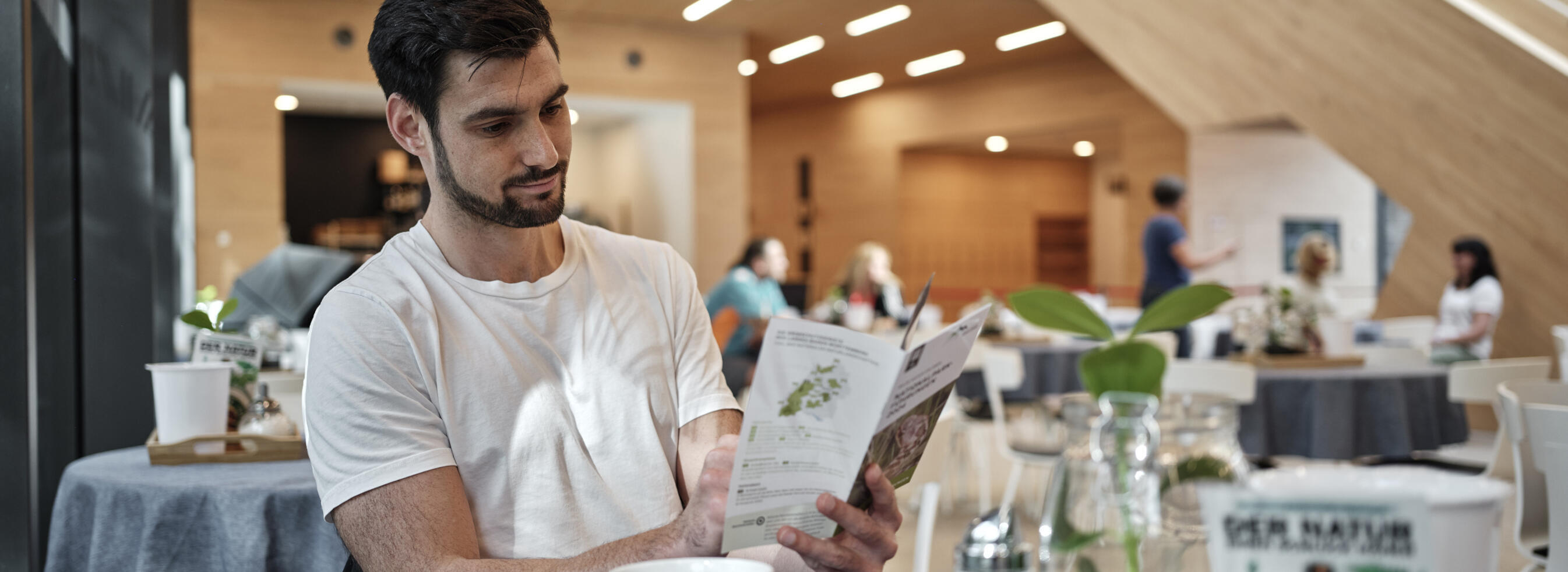 Ein Mann sitzt in einem Café und liest eine Broschüre. Foto: Christoph Duepper 