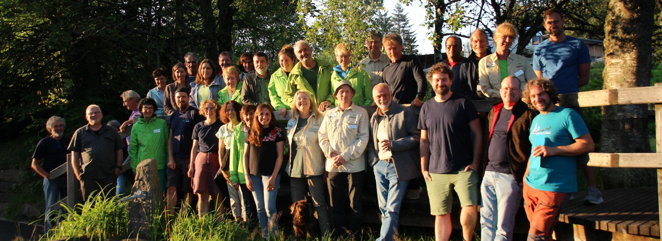 Größere Gruppe Ehrenamtlicher Rangerinnen und Ranger in sommerlicher Kleidung mit Bäumen im Hintergrund.