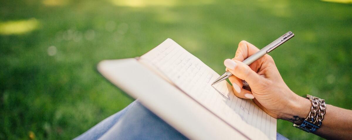 Frau schreibt in ein Notizbuch, das auf ihren Knien liegt