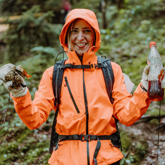 Junge Frau in orangener Regenjacke sammelt Müll im Schwarzwald