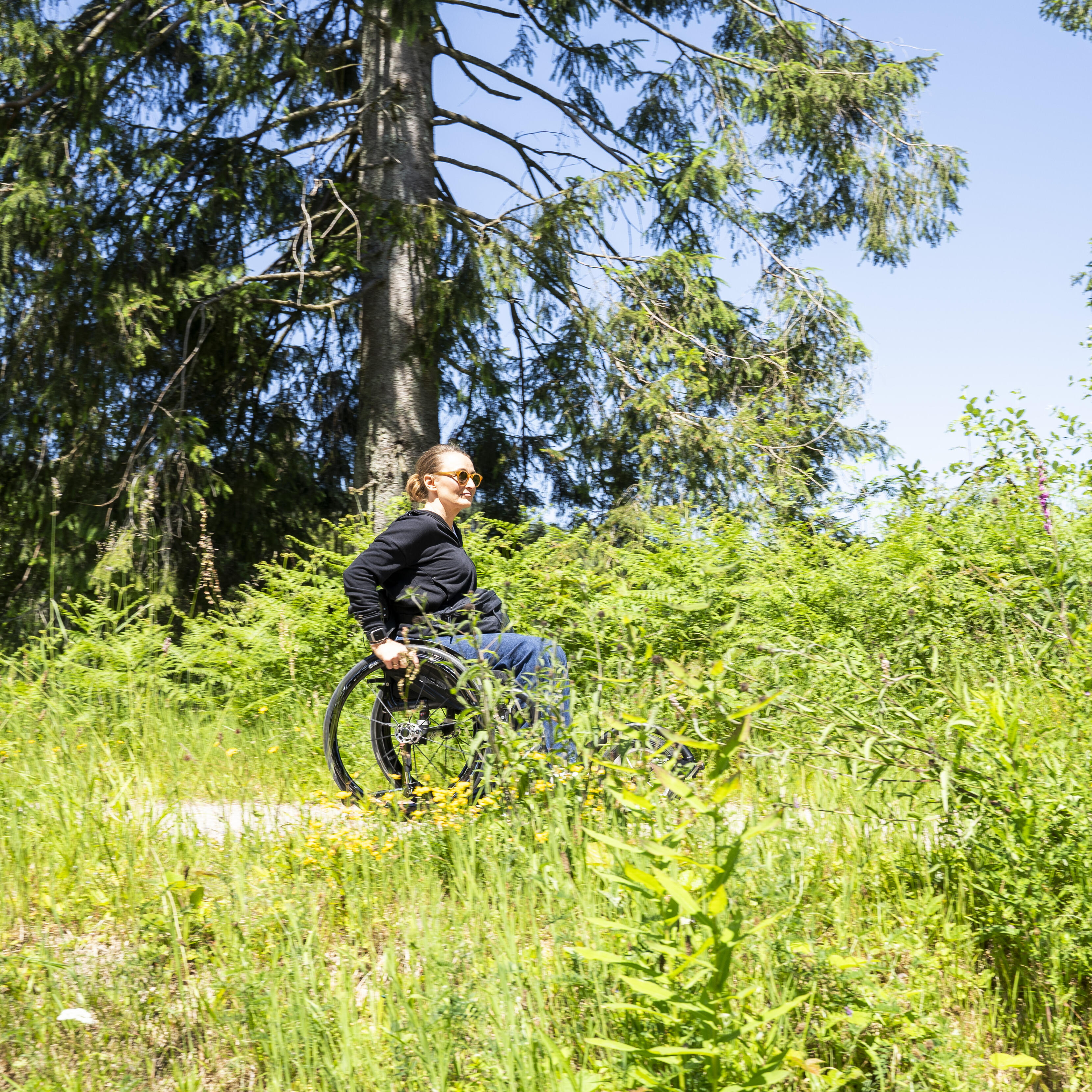 Frau fährt im Sommer mit dem Rollstuhl über einen Wanderweg