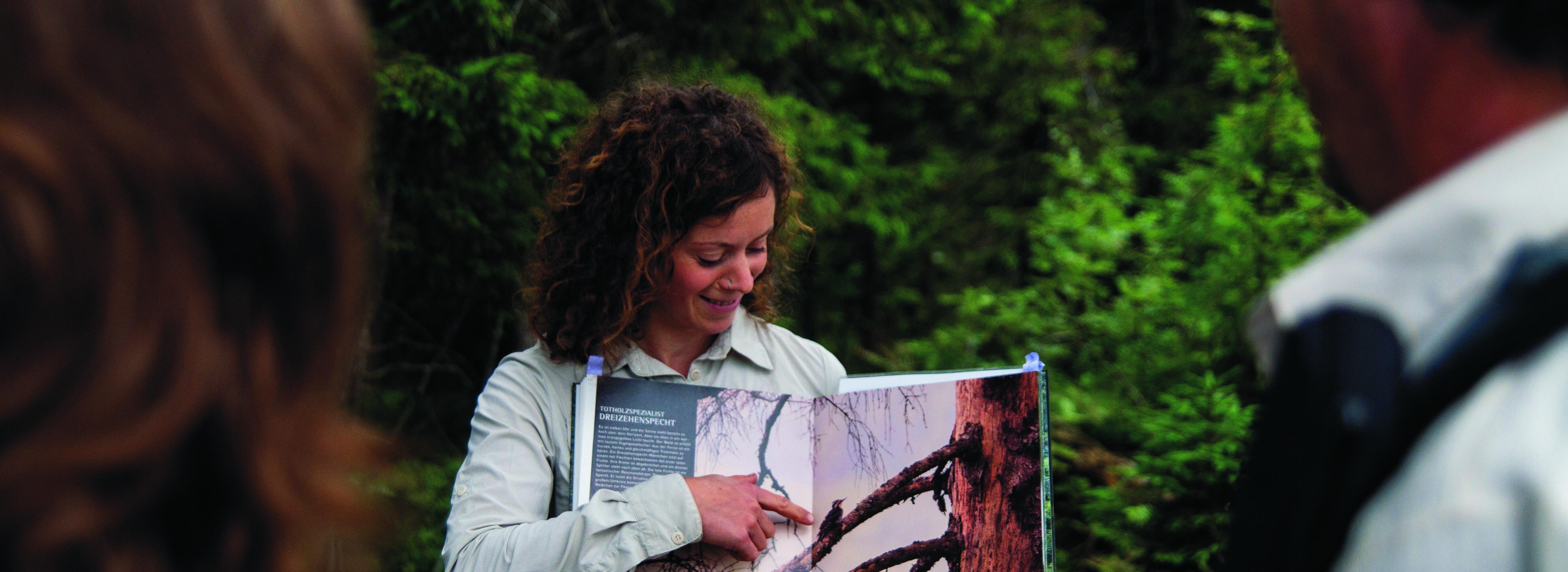 Eine Rangerin erklärt zwei Personen etwas und zeigt dabei lächelnd auf ein Bild