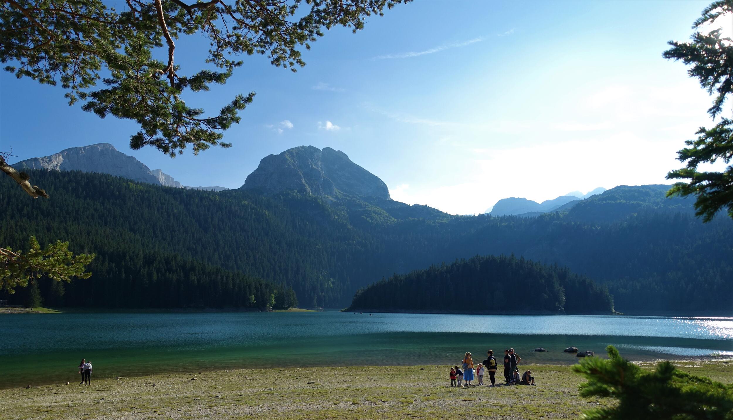 See mit Bergkulisse, eine Gruppe Menschen steht am Ufer