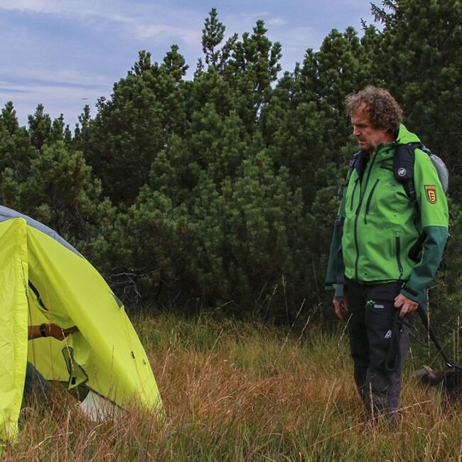 Ein Ranger steht vor einem Zelt, welches auf einer Wiese im Nationalpark steht. Dabei handelt es sich um Wild-campen was in einem Großschutzgebiet wie dem Nationalpark Schwarzwald nicht erlaubt ist.