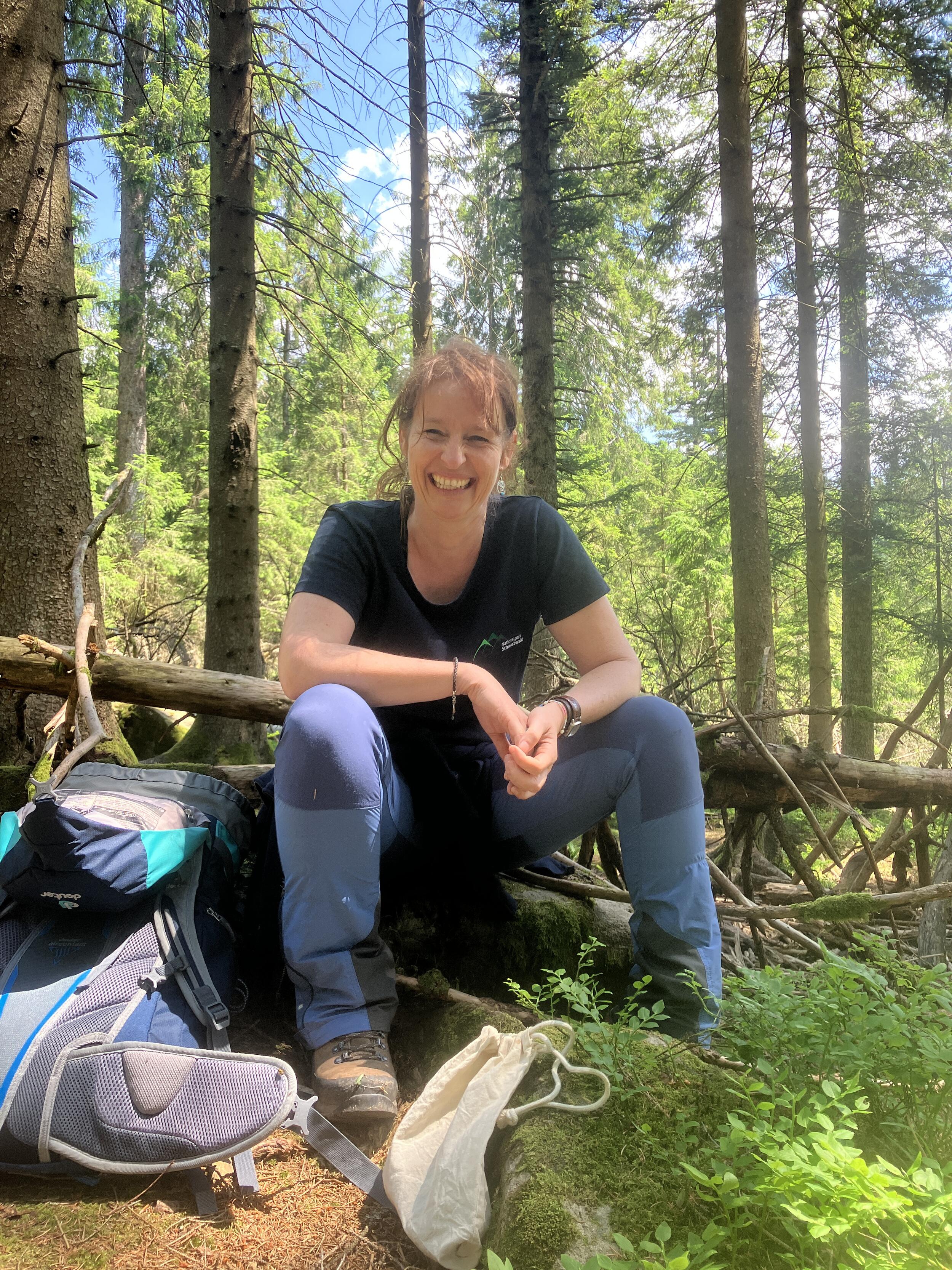 Begeistert sich für den Wald: Uli Unser. © Nina Blazon Eine Frau sitz auf einem Baumstamm und lächelt. Foto: Nina Blazon