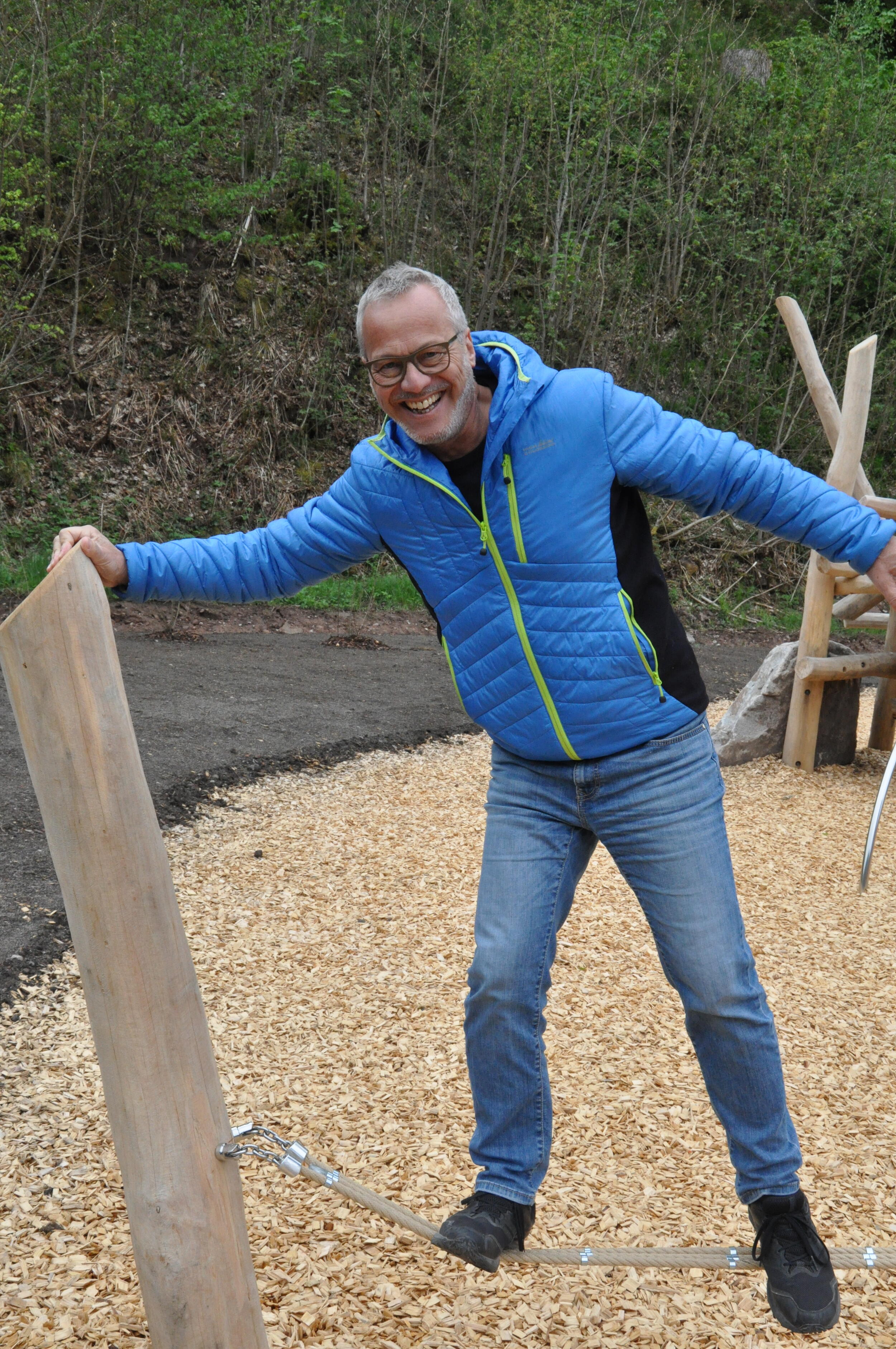Ein Mann in blauer Jacke steht auf einem Spielplatz. Er testet ein Spielgerät.   