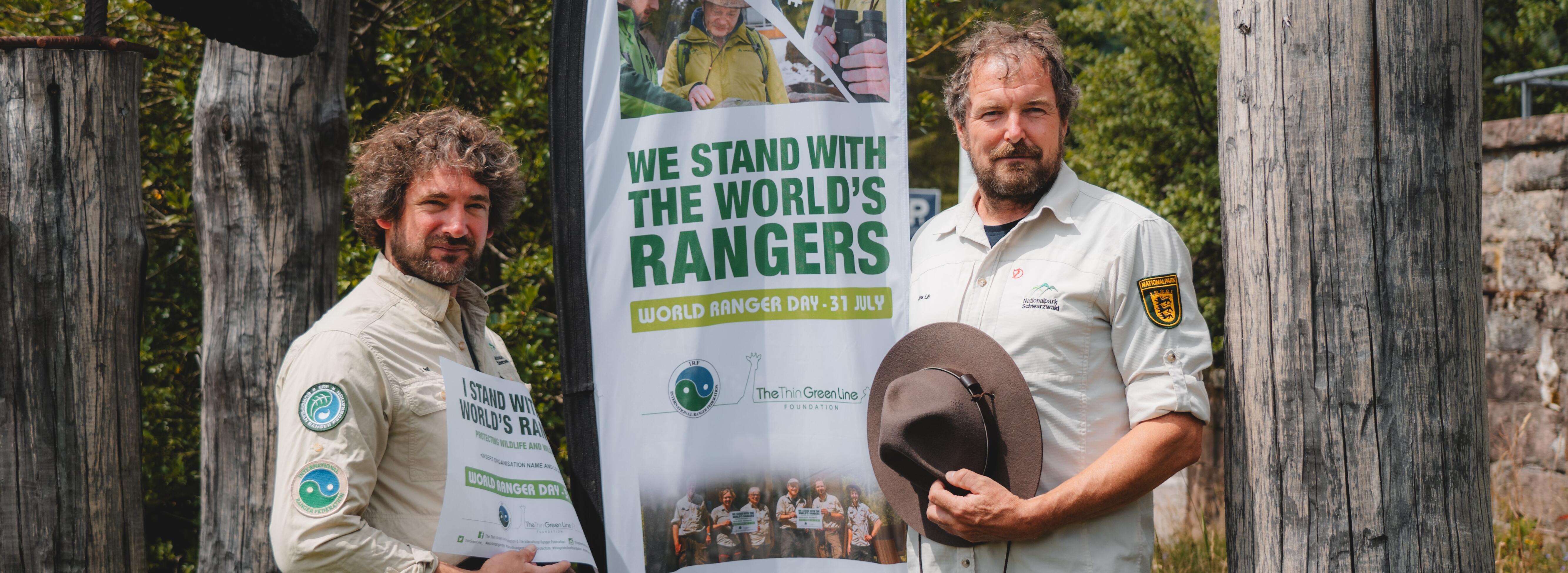 Zwei Männer in Rangeruniform vor einer Fahne mit der Aufschrift "We stand with the world's Rangers"