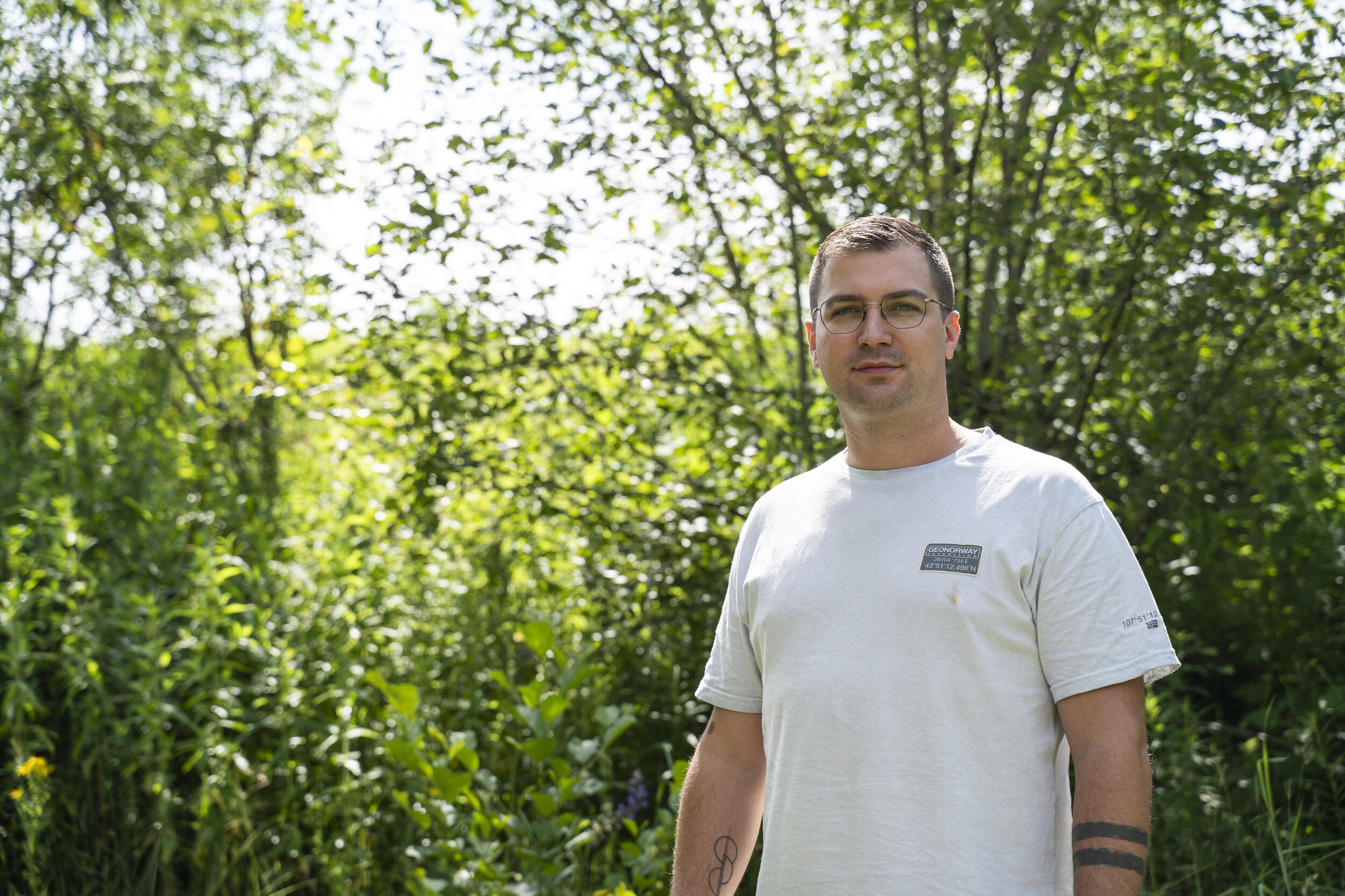 Ralph Locher. © Daniel Müller (Nationalpark Schwarzwald) Ein Mann mit Brille und weißem T-shirt steht vor grün bewachsenem Hintergrund. Foto: Daniel Müller