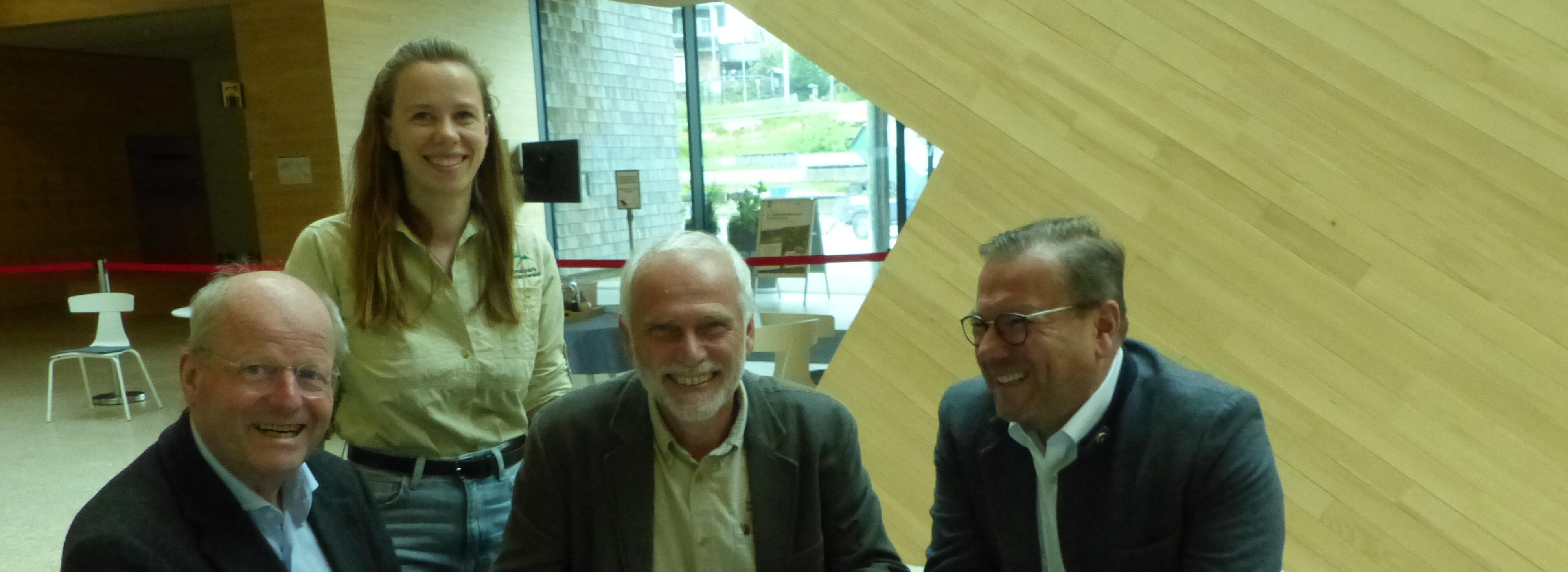 Drei Männer und eine Frau sitzen am Tisch und unterzeichnen ein Dokument.