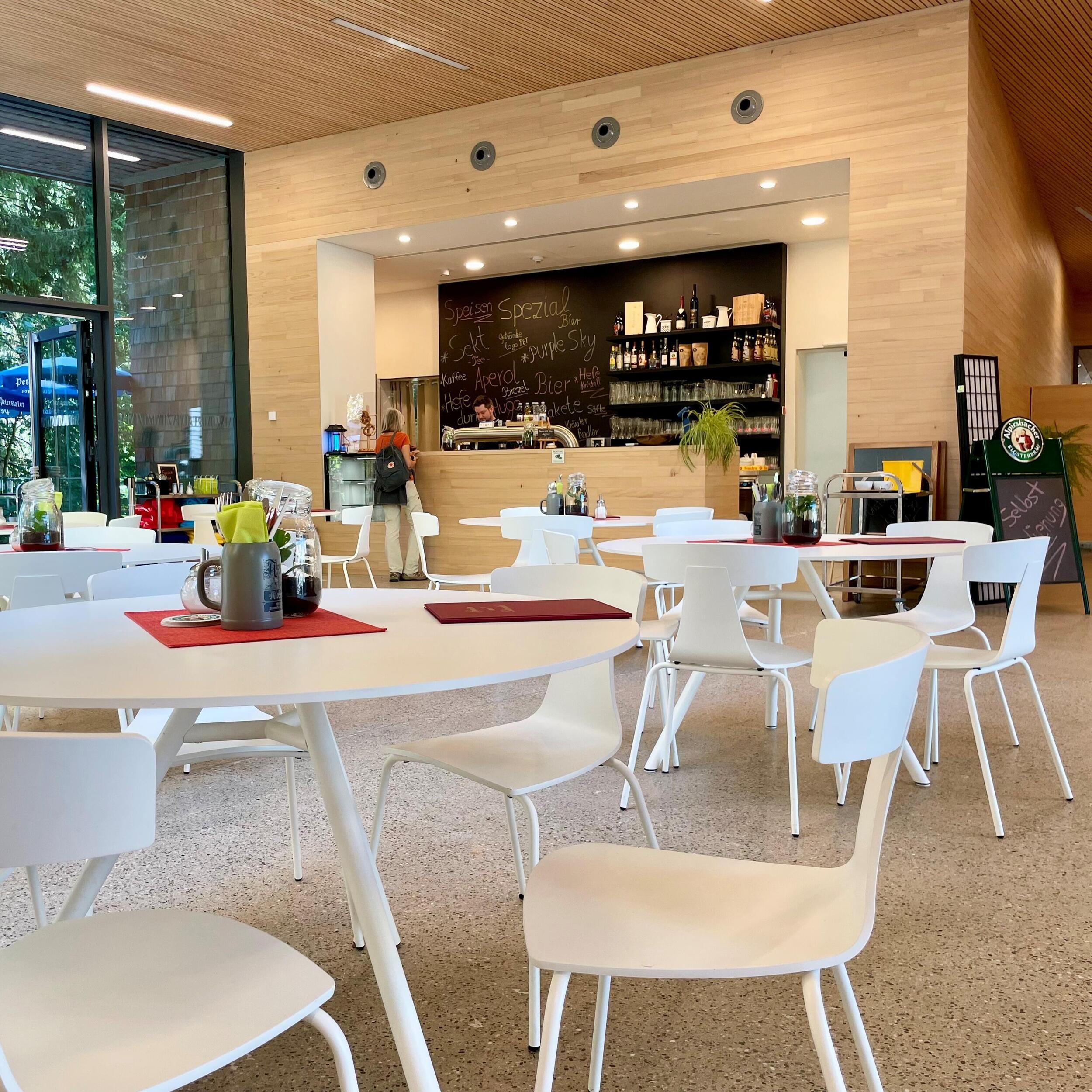 Café im Foyer Nationalparkzentrum mit offenem Thekenbereich (Stehhöhe) und weißen Tischen mit Stühlen.
