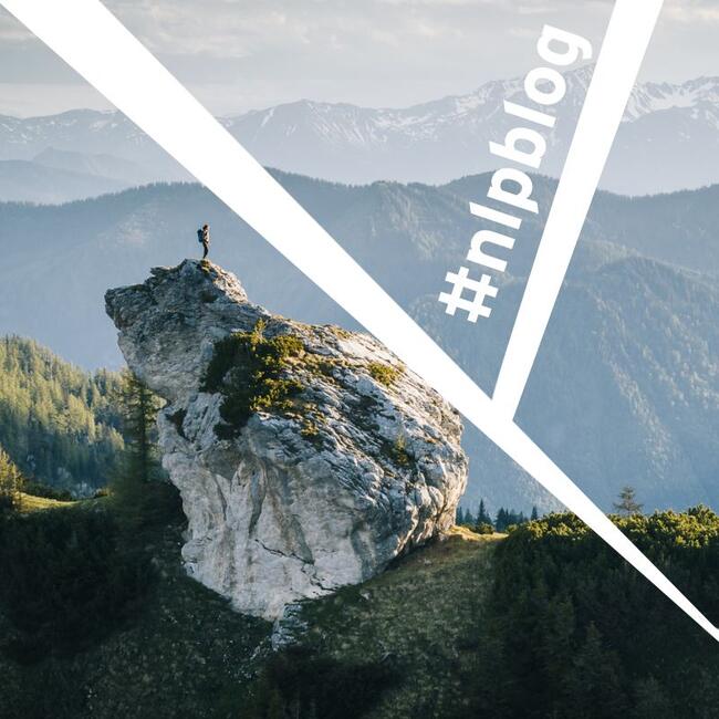 Ein großer Felsen in den Bergen. Auf dem Felsen steht ein Mensch mit einem Rucksack. Im Hintergrund sind Berge. Foto: Simon Straetker