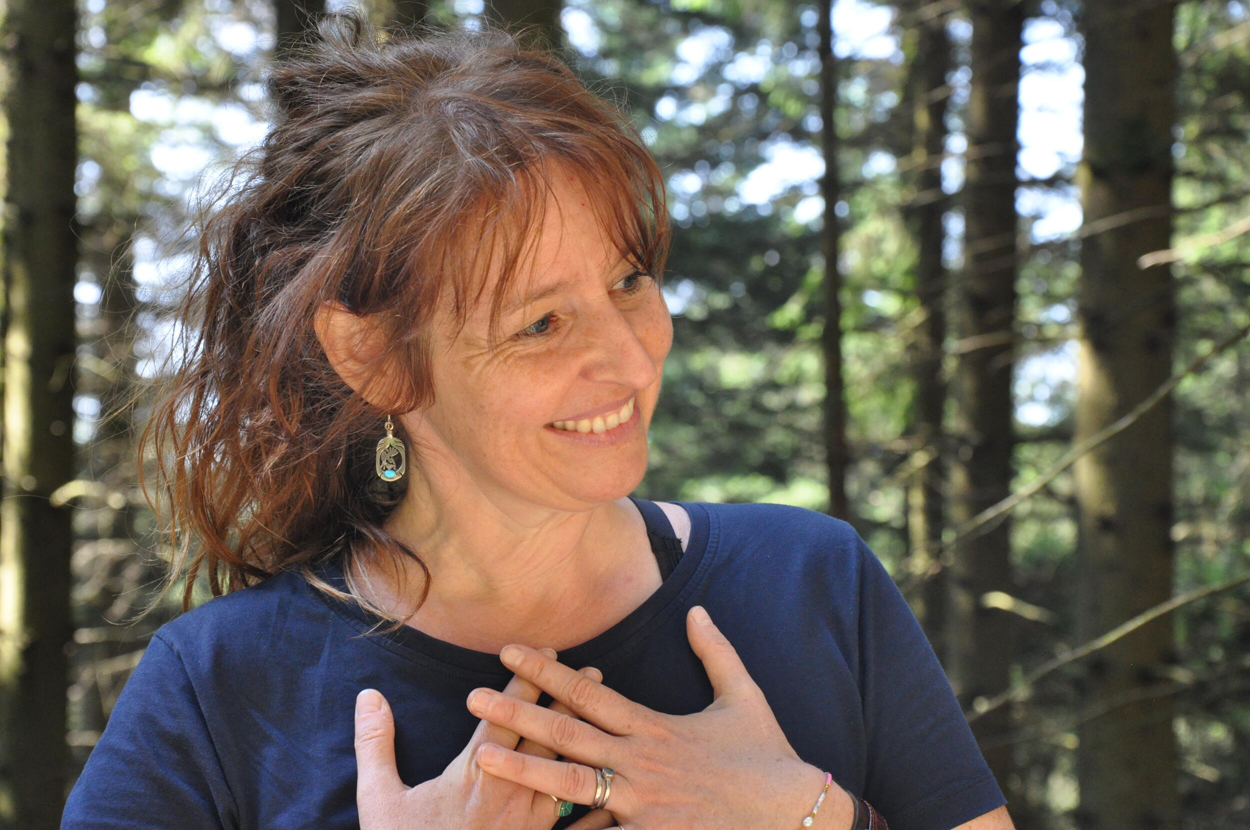 Uli Unser, Lehrerin im Gymnasium und Wildnis-Pädagogin. © Nina Blazon Eine Frau in blauem T-Shirt schaut zur Seite und lächelt. Sie hält die Hände auf der Brust. Foto: Nina Blazon