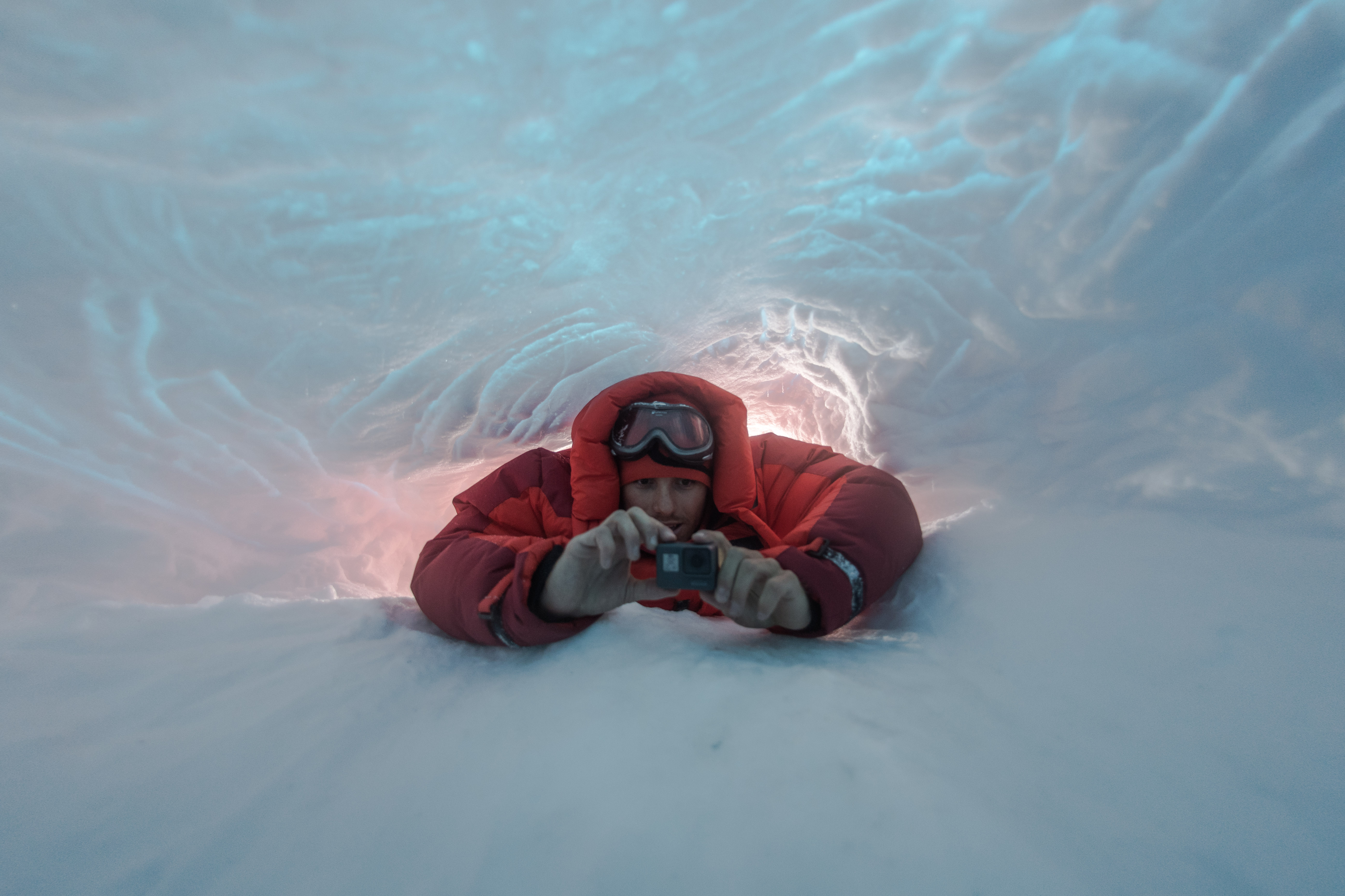 Ein Mann im roten Schneeanzug liegt auf dem Schnee. Er hält eine Kamera in der Hand. Foto: Markus Mauthe 