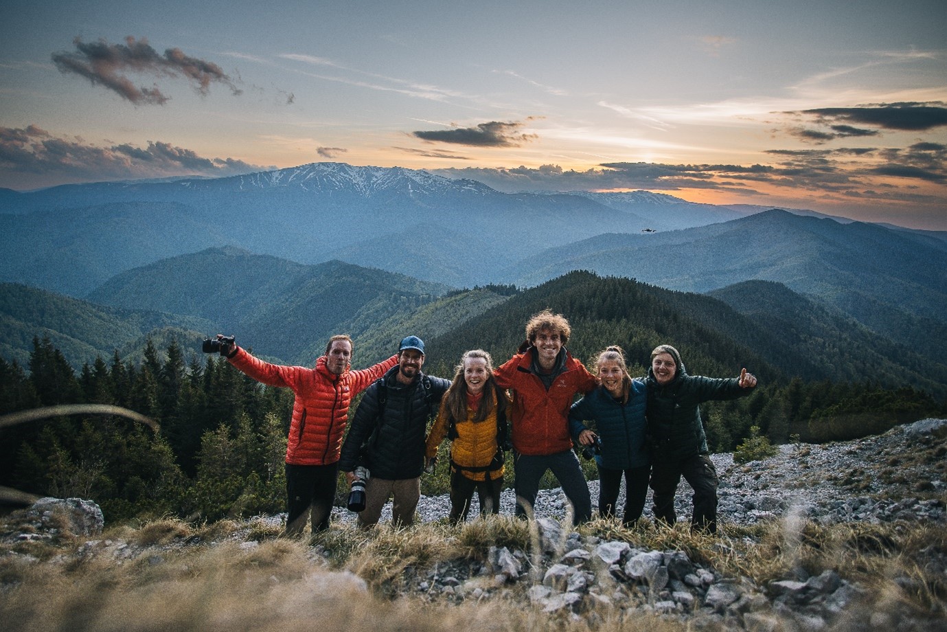 Eine Gruppe Menschen steht vor Bergen. Sie lächeln. Im Hintergrund geht die Sonne runter.  Foto: Wild Europe e.V.