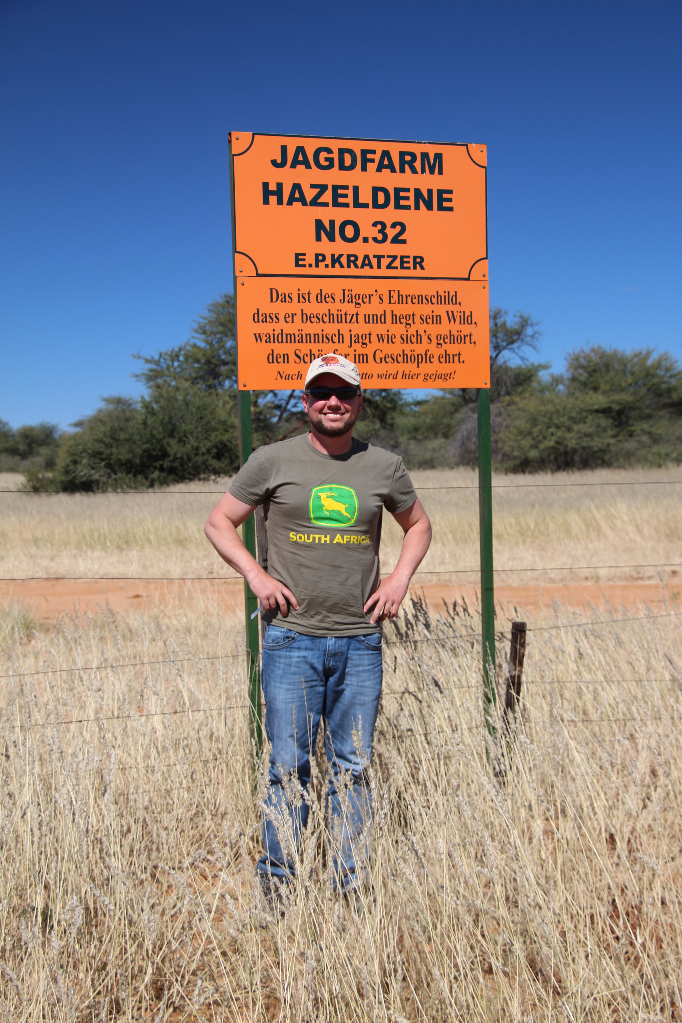 Ein Mann mit Mütze steht vor einem orangefarbenen Schild auf einer Weidefläche. Foto: Nina Zeiler