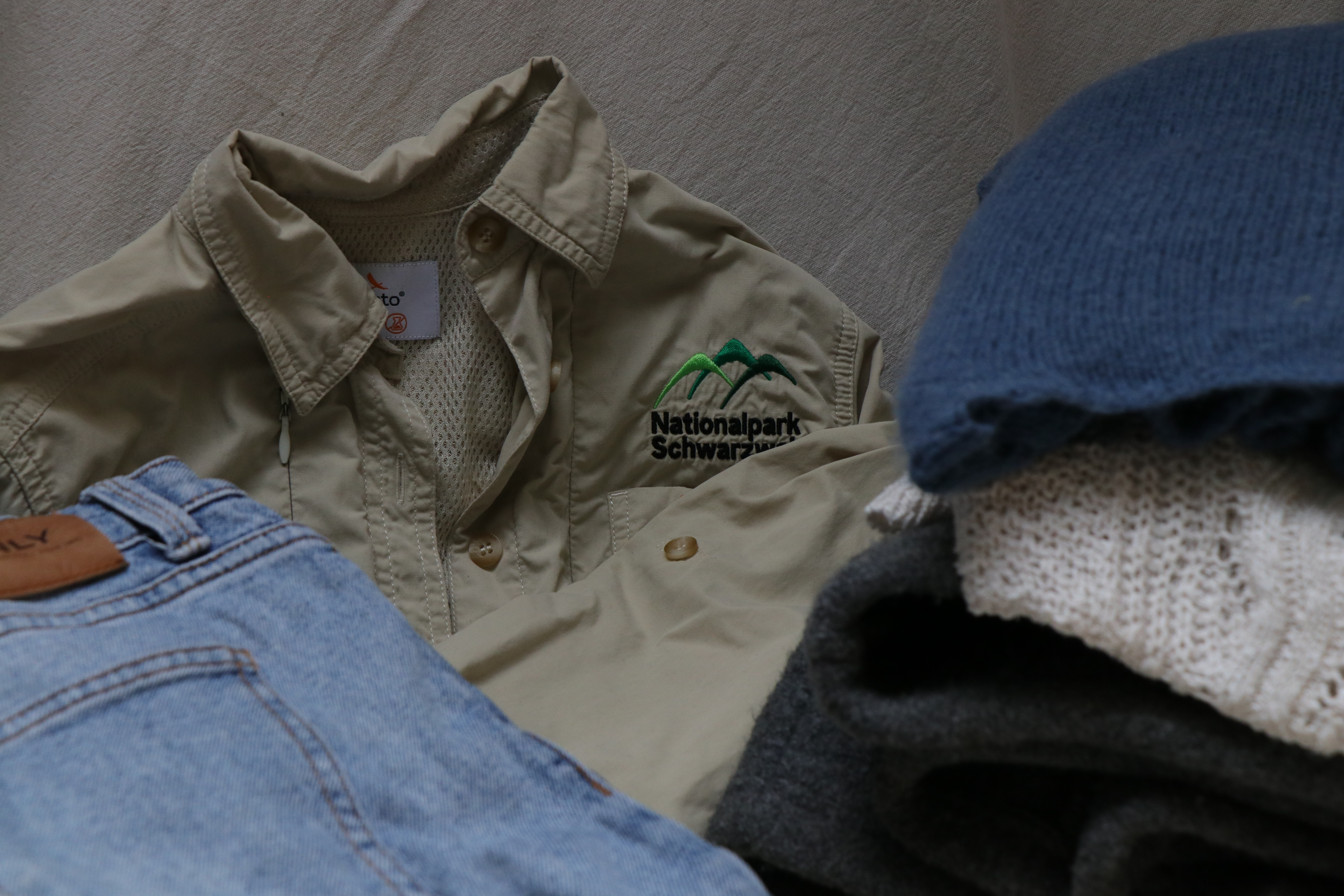 Hemd, Jeans, Mütze und andere Kleidungsstücke liegen zusammengelegt auf einem Bett